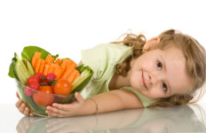 Little girl leaning on the table with a bowl of vegetables - isolated